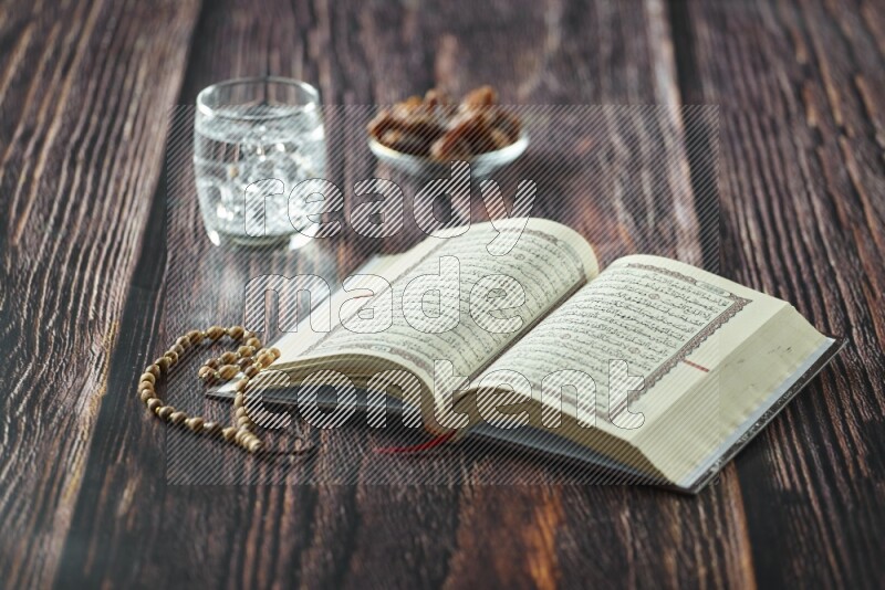 Quran with dates, prayer beads and different drinks all placed on wooden background