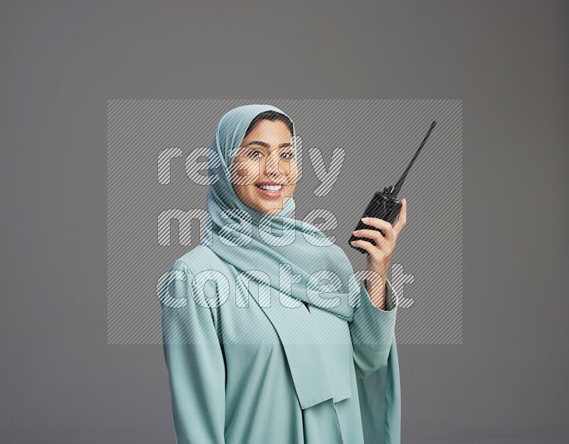 Saudi Woman wearing Abaya standing holding walkie-talkie on Gray background