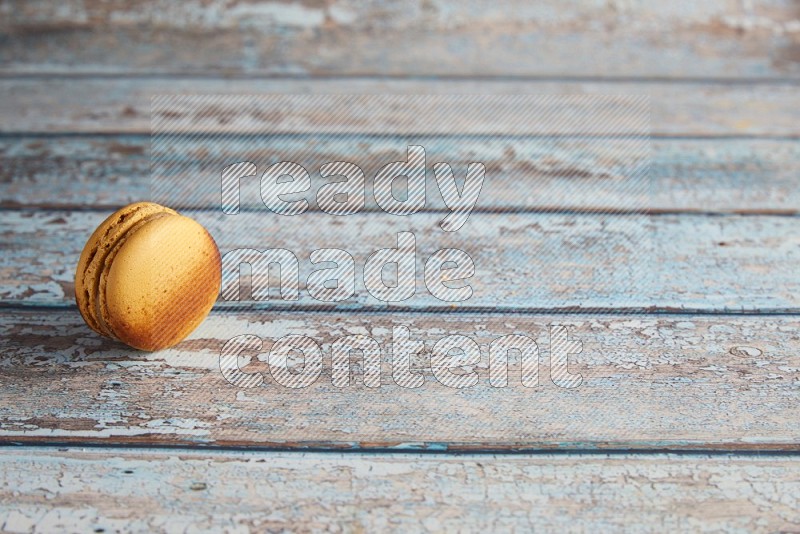 45º Shot of Yellow Crème Brulée macaron on light blue wooden background