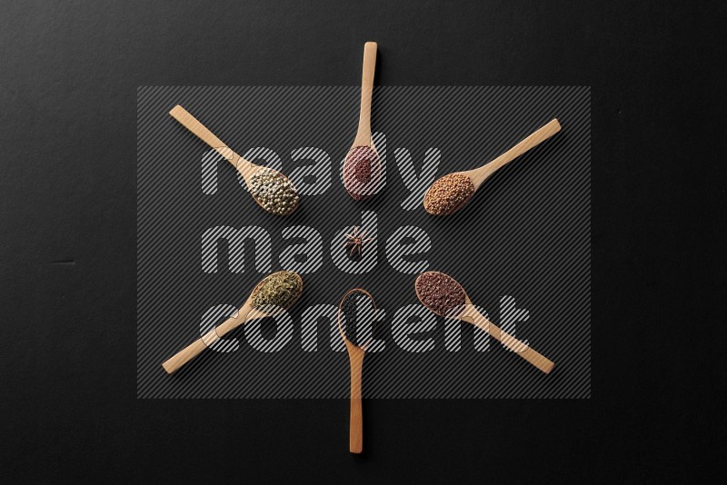 wooden spoons filled with white peppers, mustard seeds, black seeds, garden cress, cumin and flax on black flooring and shaped like a clock