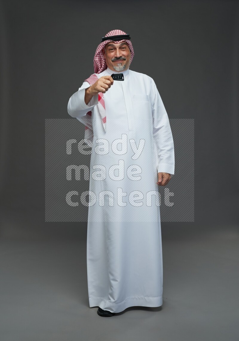 Saudi man with shomag Standing holding car key on gray background