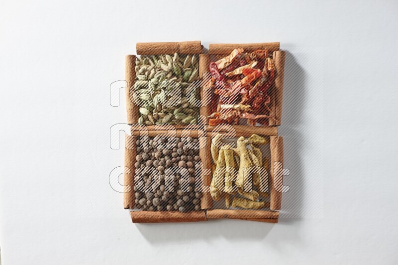 4 مربعات من أعواد القرفة ممتلئة بالفلفل الأحمر المجفف والهيل وأصابع الكركم وبهار الفلفل الحلو على أرضية بيضاء