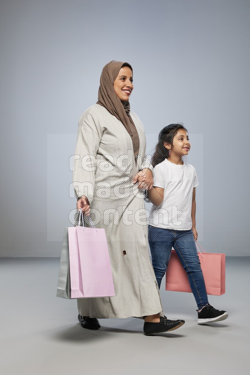 Mom and daughter holding shopping bags on gray background