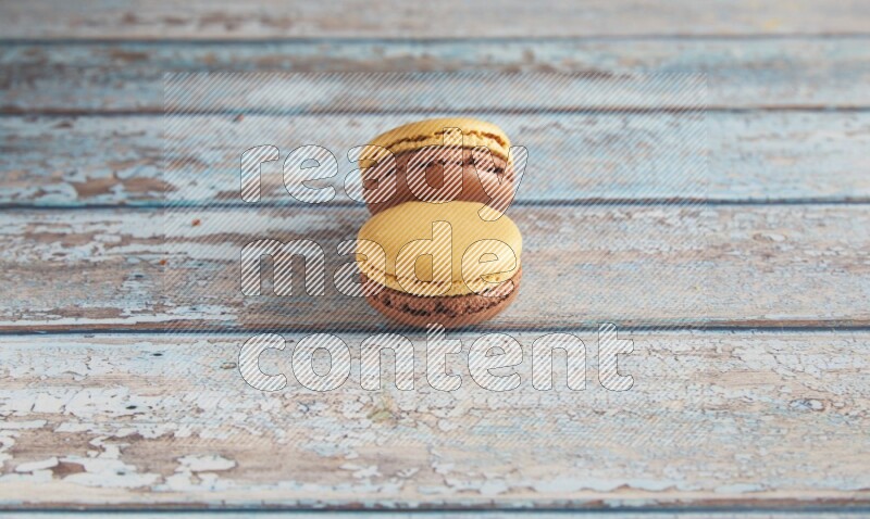 45º Shot of two Yellow and Brown Chai Latte macarons on light blue wooden background