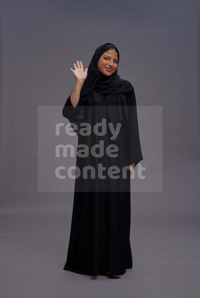 Saudi woman wearing Abaya standing interacting with the camera on gray background