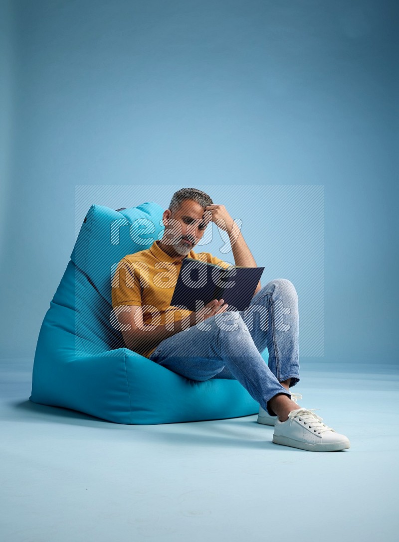 A man sitting on a blue beanbag and reading a book