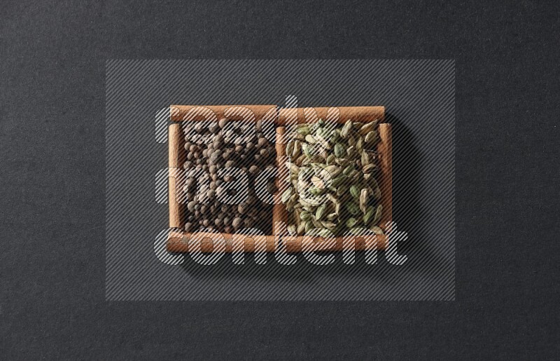 مربعان من أعواد القرفة ممتلئان ببهار الفلفل الحلو وحب الهيل علي خلفية سوداء