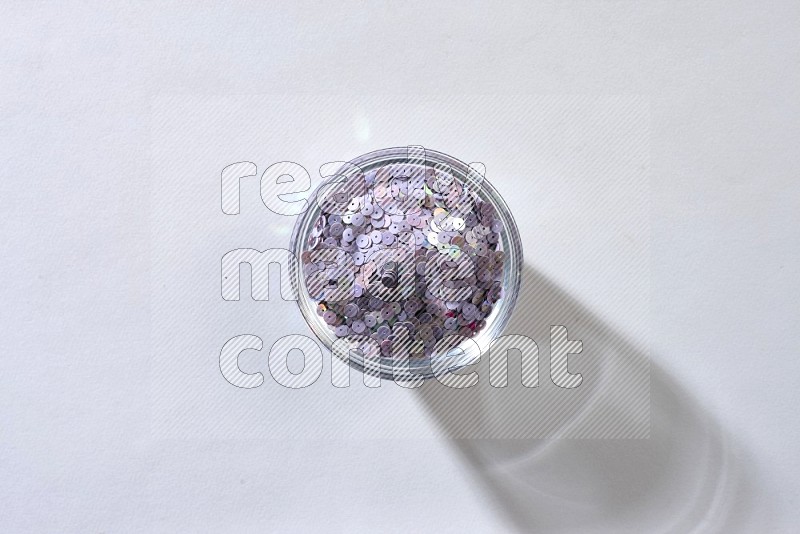 A glass bowl full of colored flat sequins on grey background