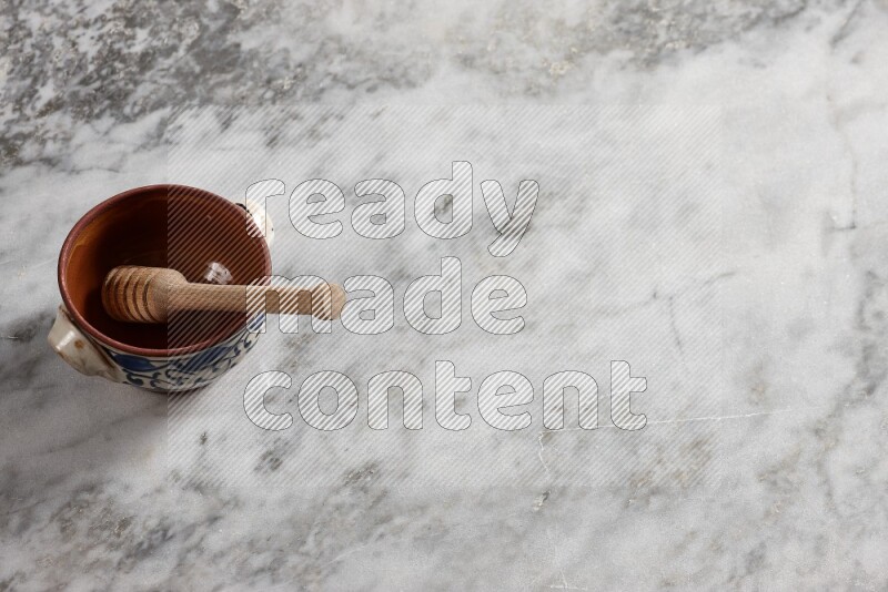 Decorative pottery pot with wooden honey dipper in it on grey marble background