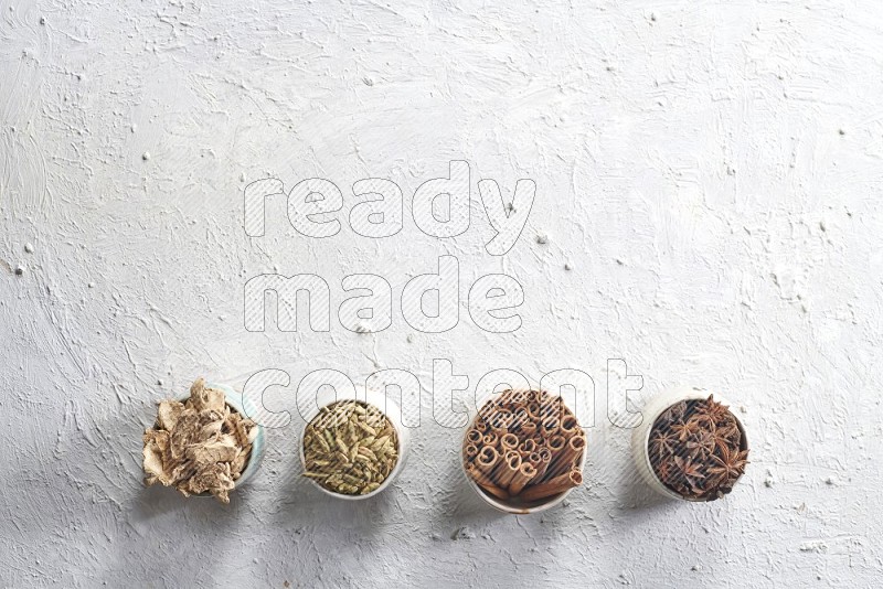 Cardamom, ginger, cinnamon sticks and star anise in 4 bowls on a textured white background
