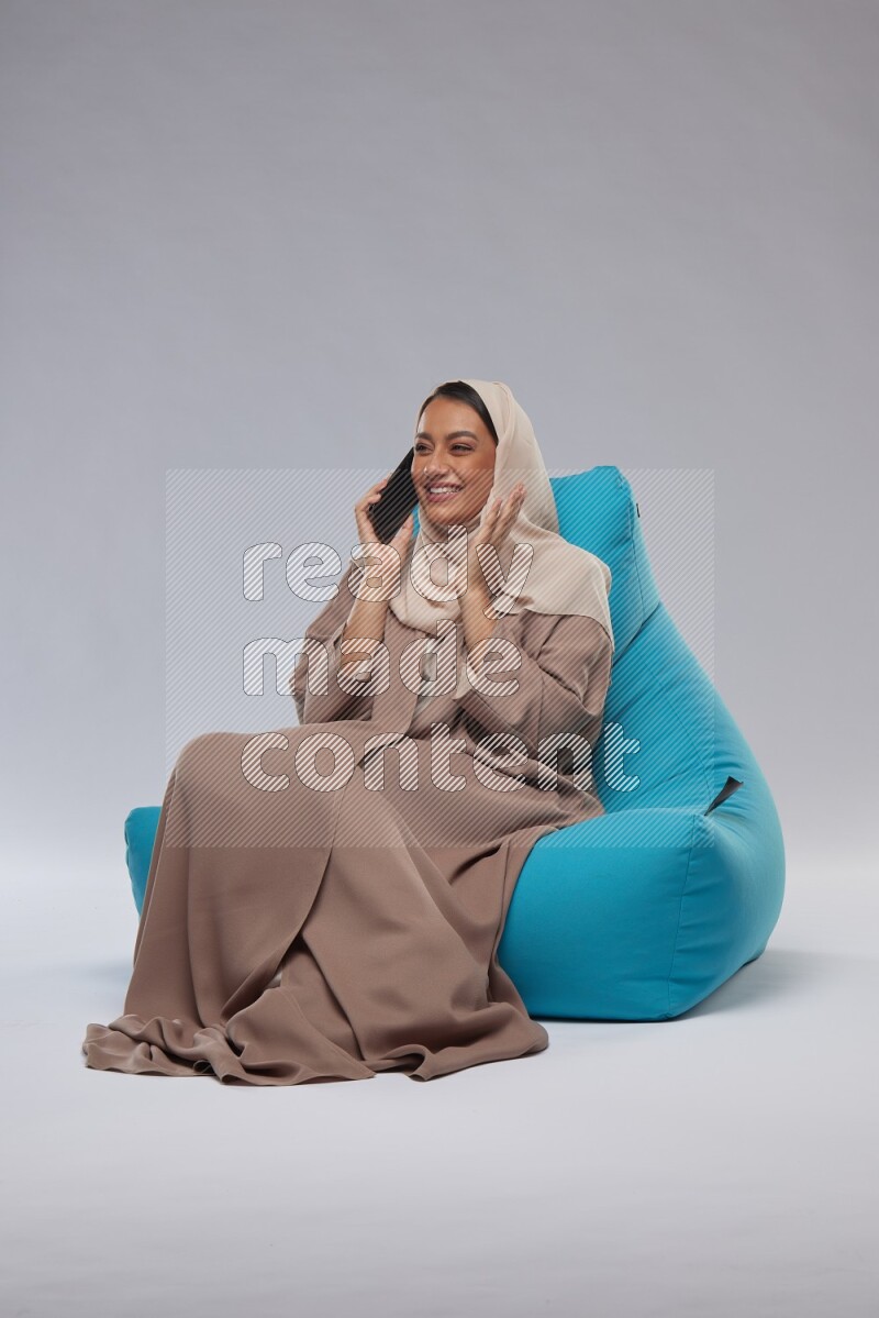 A Saudi woman sitting on a blue beanbag and working on laptop