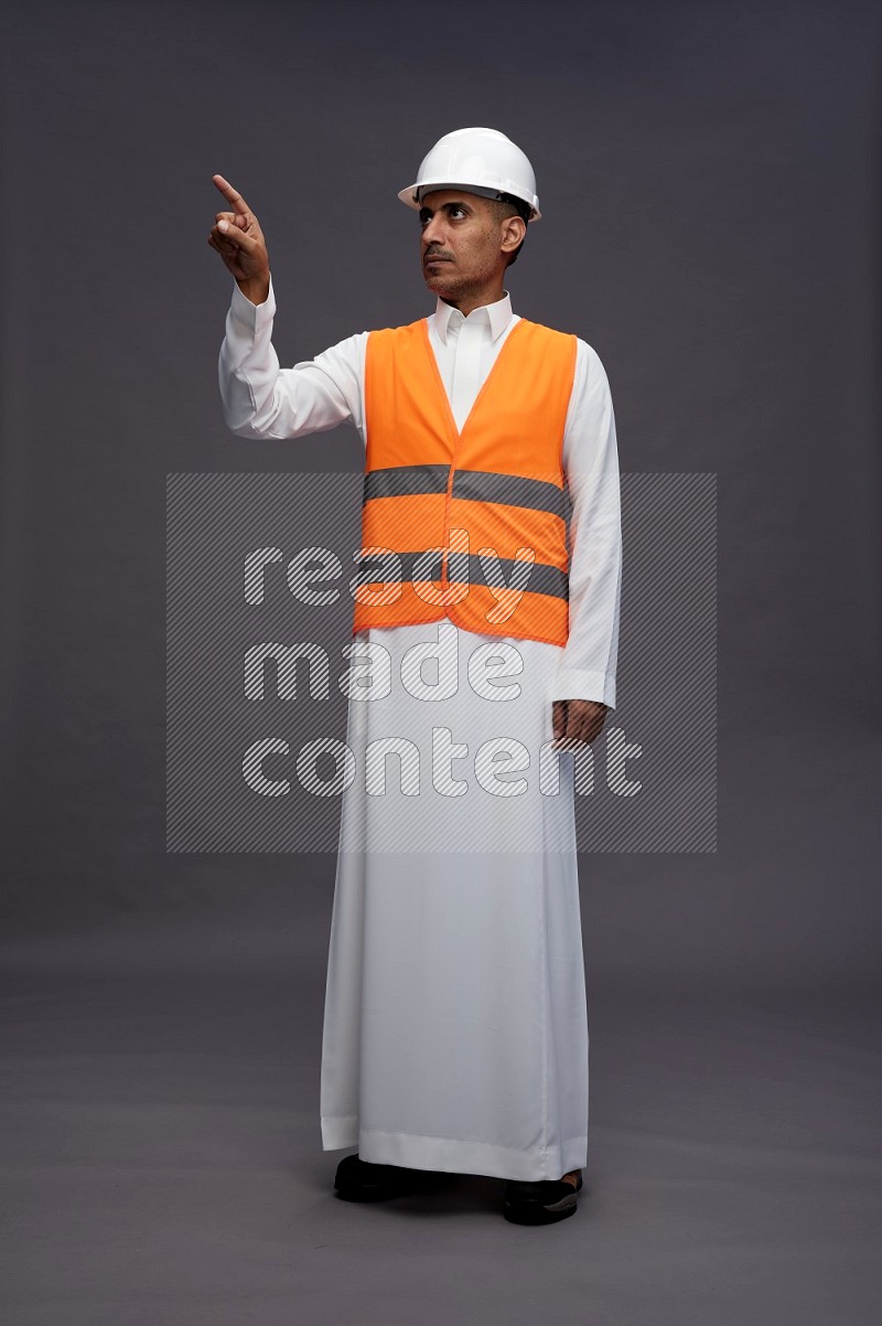 Saudi man wearing thob with engineer vest standing interacting with the camera on gray background