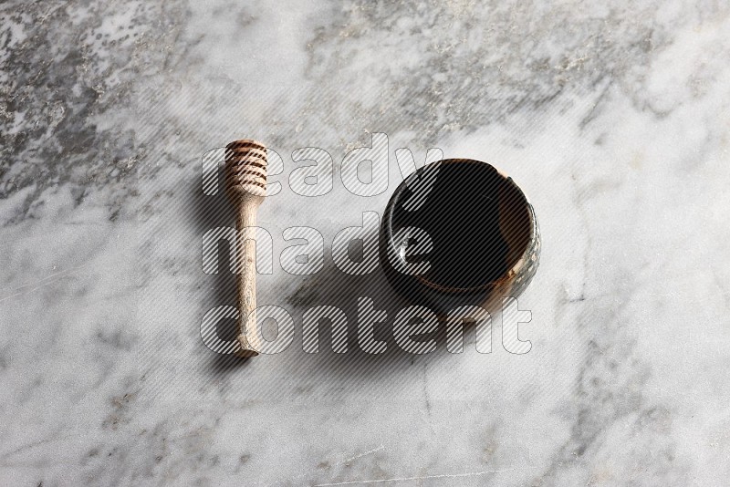 Multicolored Pottery bowl with wooden honey handle on the side with grey marble flooring, 65 degree angle