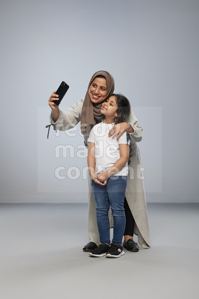 A girl standing taking selfie with her mother on gray background
