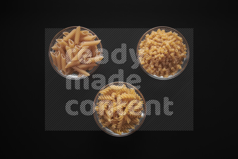 Different pasta types in glass bowls on black background