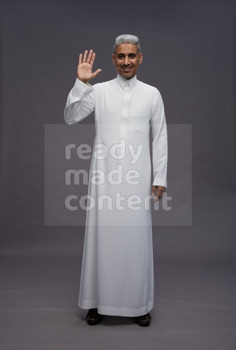 Saudi man wearing thob standing interacting with the camera on gray background