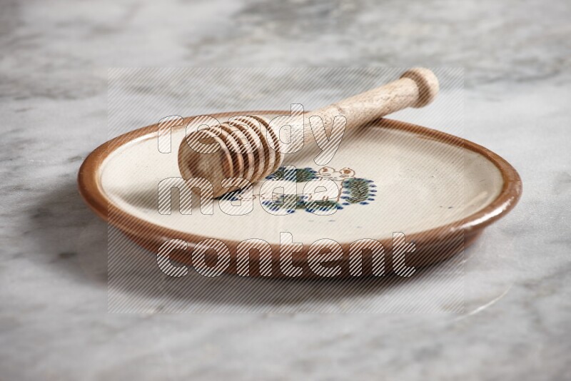 Decorative pottery plate with wooden honey dipper in it on grey marble background