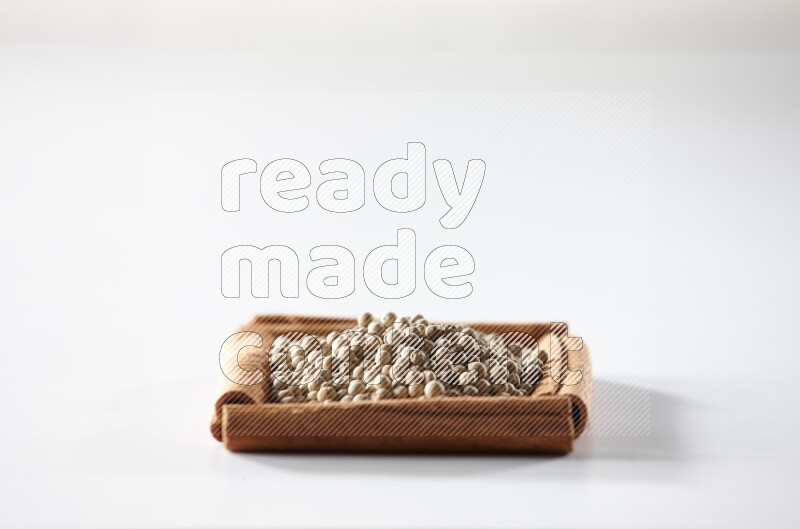 أربعة من أعواد القرفة مكونة شكل مربع بداخلها حبوب الفلفل الأبيض علي خلفية بيضاء