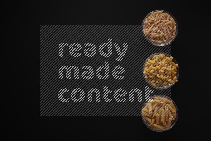 Different pasta types in 3 glass bowls on black background