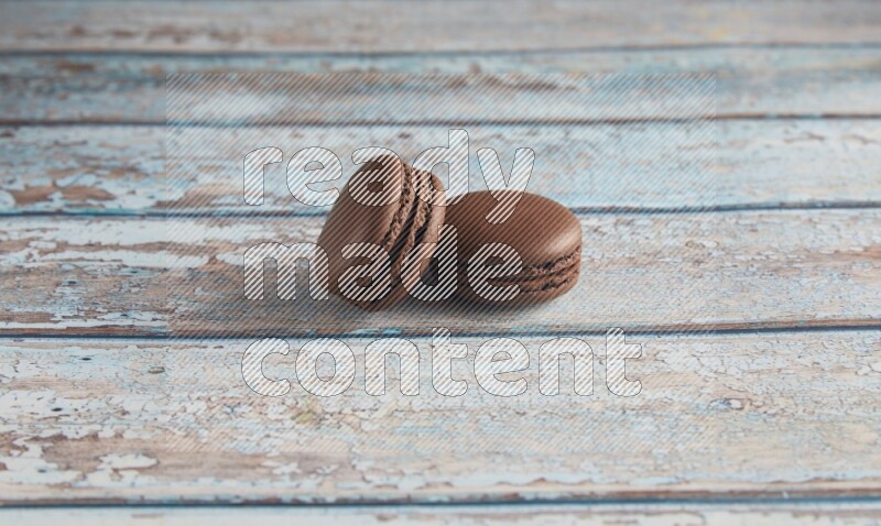 45º Shot of two Brown Dark Chocolate macarons on light blue wooden background