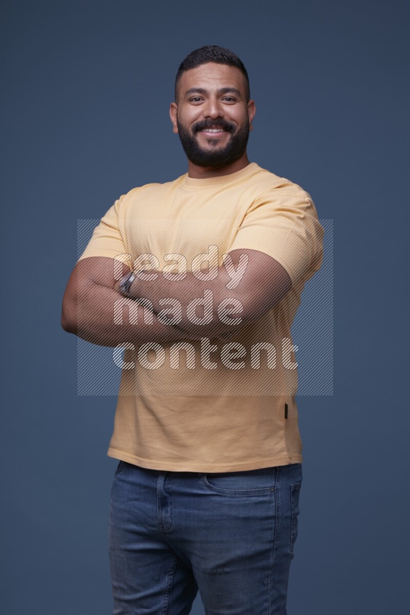 A man posing in a blue background wearing a yellow shirt