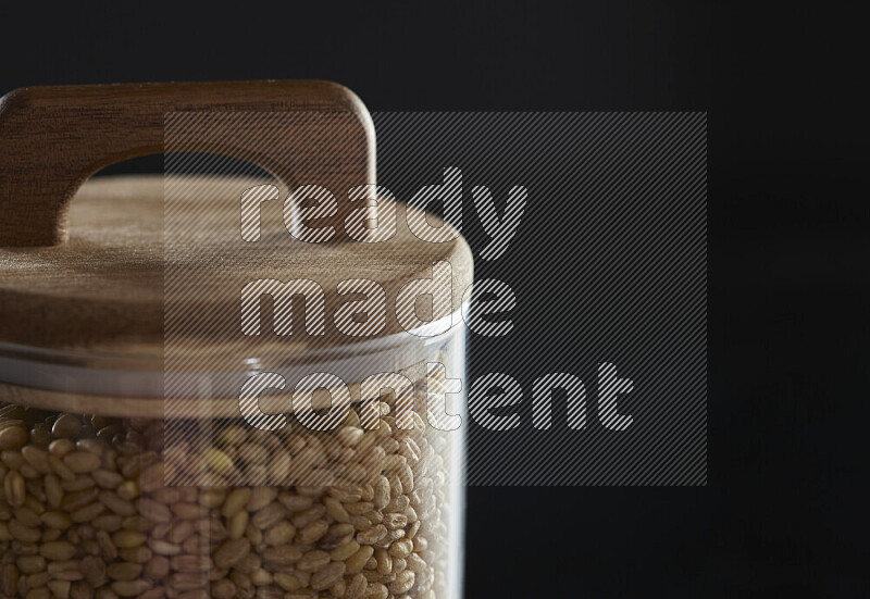 Hulled wheat in a glass jar on black background