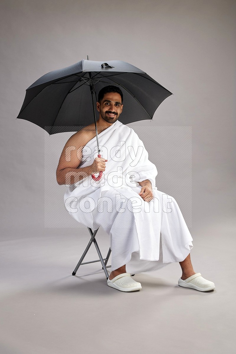 A man wearing Ehram with face mask Standing holding umbrella on gray background