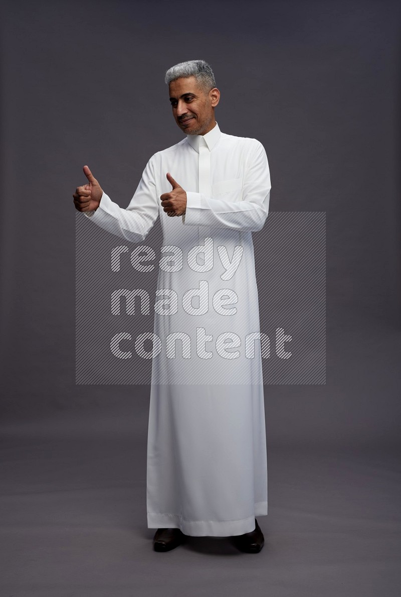 Saudi man wearing thob standing interacting with the camera on gray background