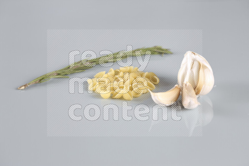 Raw pasta with different ingredients such as cherry tomatoes, garlic, onions, red chilis, black pepper, white pepper, bay laurel leaves, rosemary, cardamom and mushrooms on light blue background