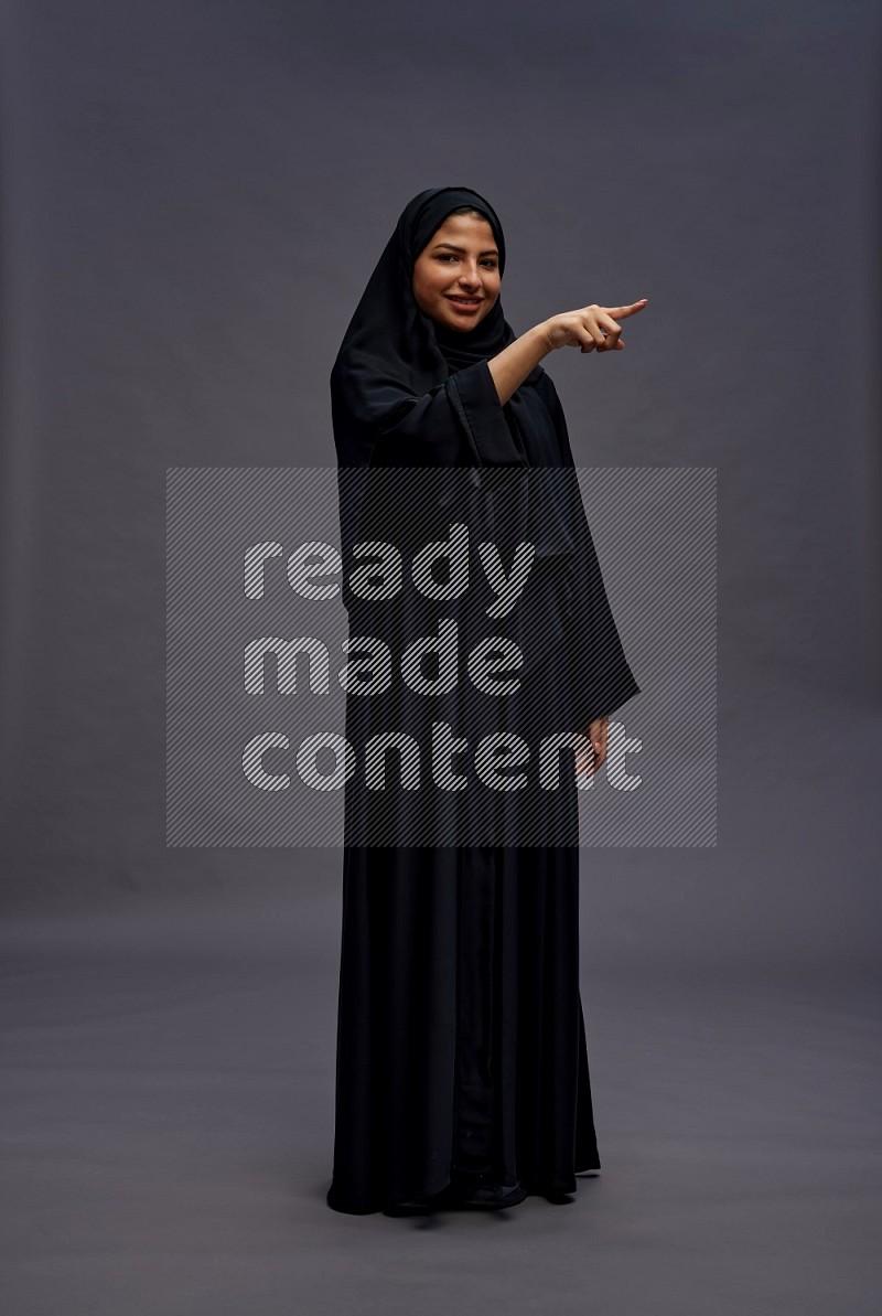 Saudi woman wearing Abaya standing interacting with the camera on gray background