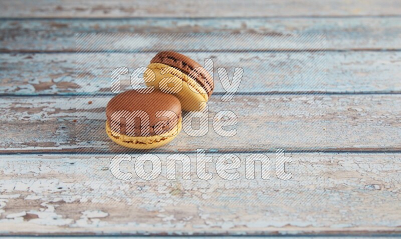 45º Shot of two Yellow and Brown Chai Latte macarons on light blue wooden background