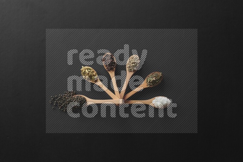 الفلفل الأبيض والقرنفل والهيل والملح والفلفل الأسود وريحان مجفف في معالق خشبية علي خلفية سوداء