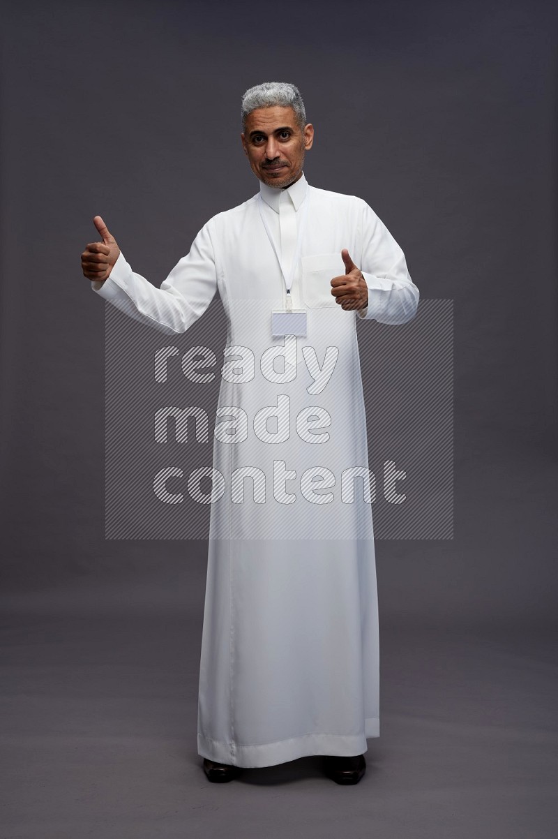 Saudi man wearing thob with neck strap employee badge standing interacting with the camera on gray background