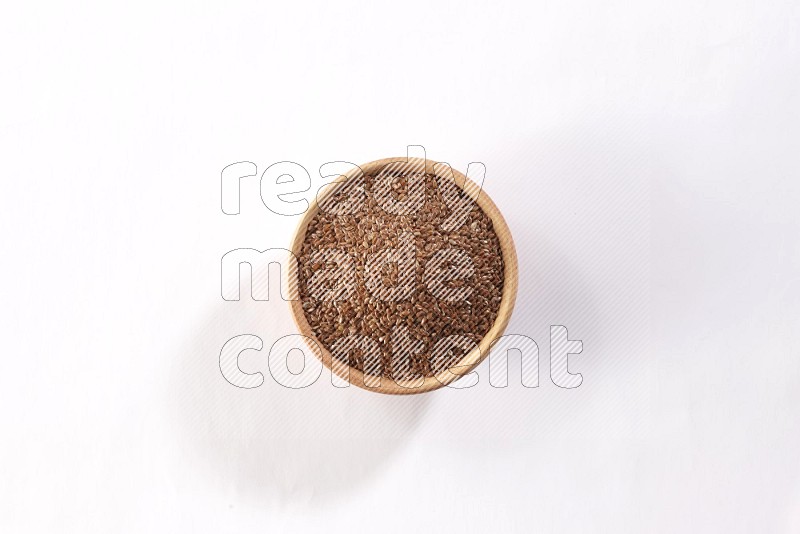 A wooden bowl full of flax seeds on a white flooring