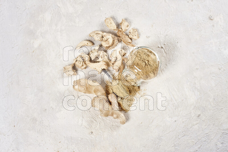 A glass jar full of ground ginger powder flipped with some spilling powder on white background