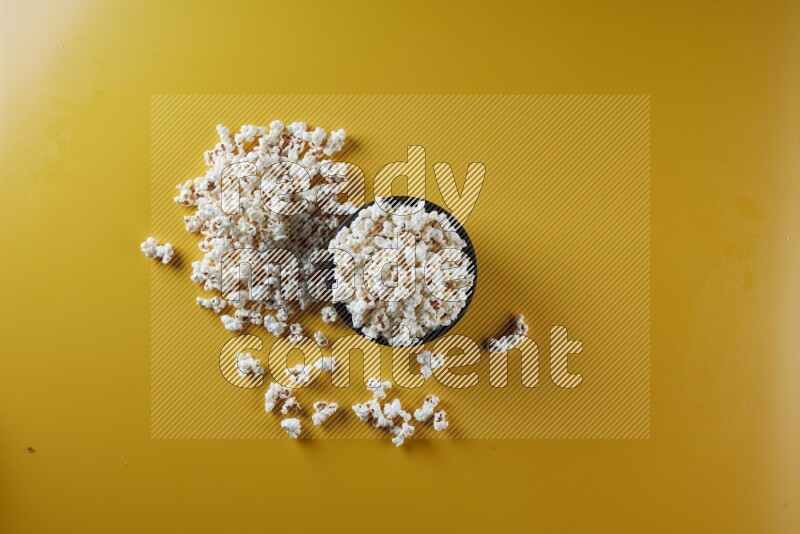 A black ceramic bowl full of popcorn with popcorn beside it on a yellow background in different angles