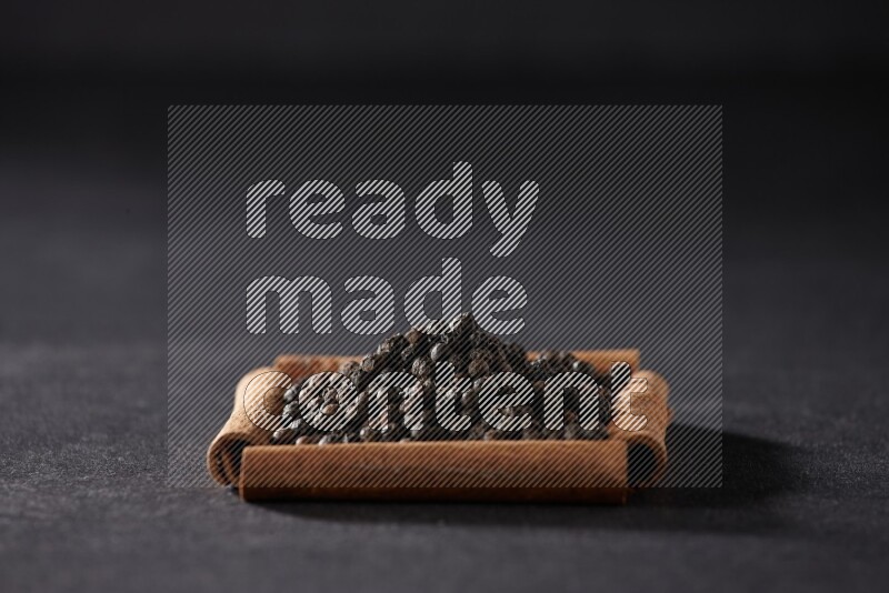 أربعة من أعواد القرفة مكونة شكل مربع بداخلها حبوب الفلفل الأسود علي خلفية سوداء