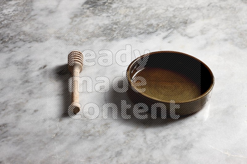 Multicolored Pottery oven plate with wooden honey handle on the side with grey marble flooring, 45 degree angle