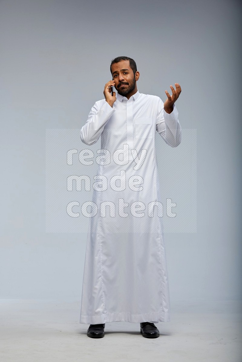 Saudi man wearing Thob standing talking on phone on Gray background