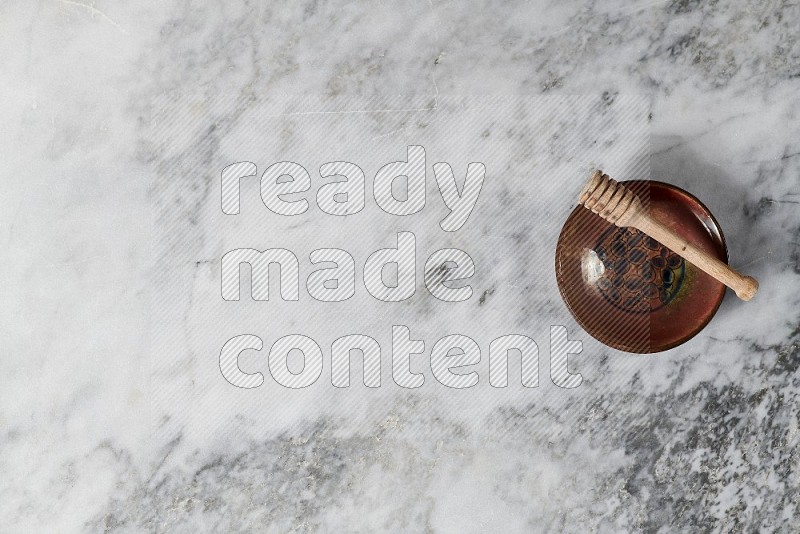 Decorative Pottery Plate with wooden honey handle in it, on grey marble flooring, Top View