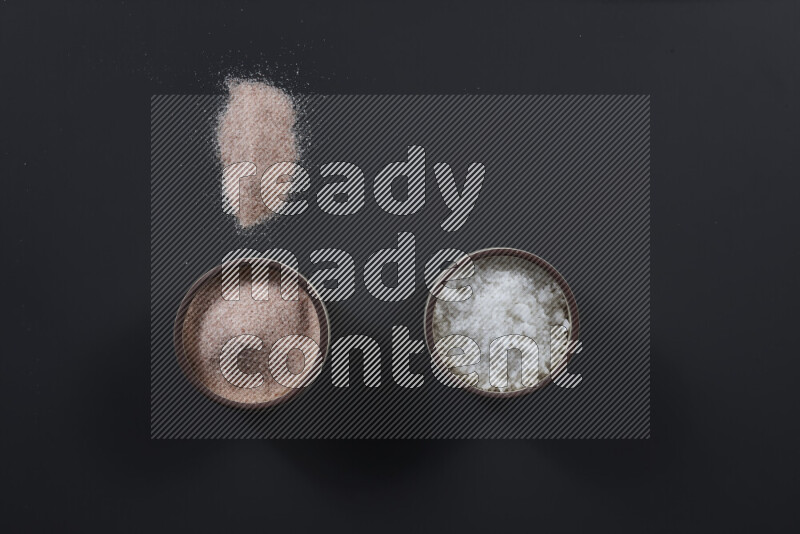 2 وعاء فخاري احدهمها ممتلئ بملح الهيمالايا والأخر بالملح الأبيض على خلفية سوداء