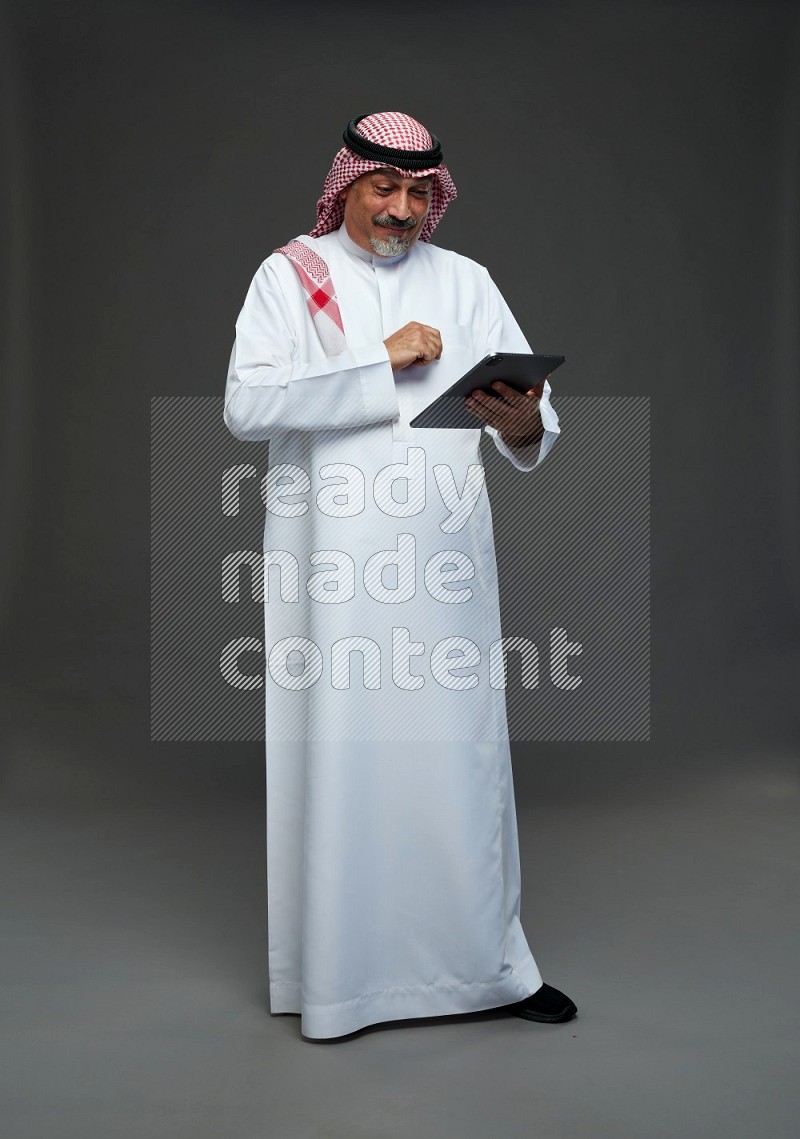 Saudi man with shomag Standing working on tablet on gray background