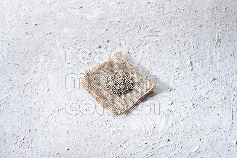 White pepper beads on a burlap piece of fabric on textured white flooring