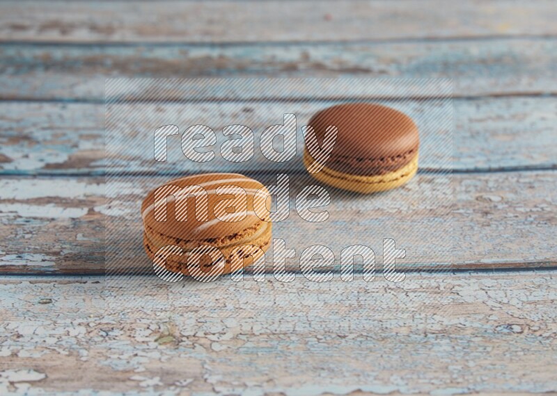45º Shot of of two assorted Brown Irish Cream, and Yellow, and Brown Chai Latte macarons  on light blue background