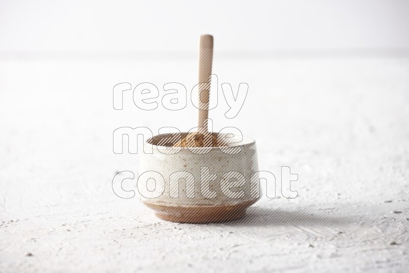 Ceramic beige bowl full of cinnamon powder with a wooden spoon on a textured white background