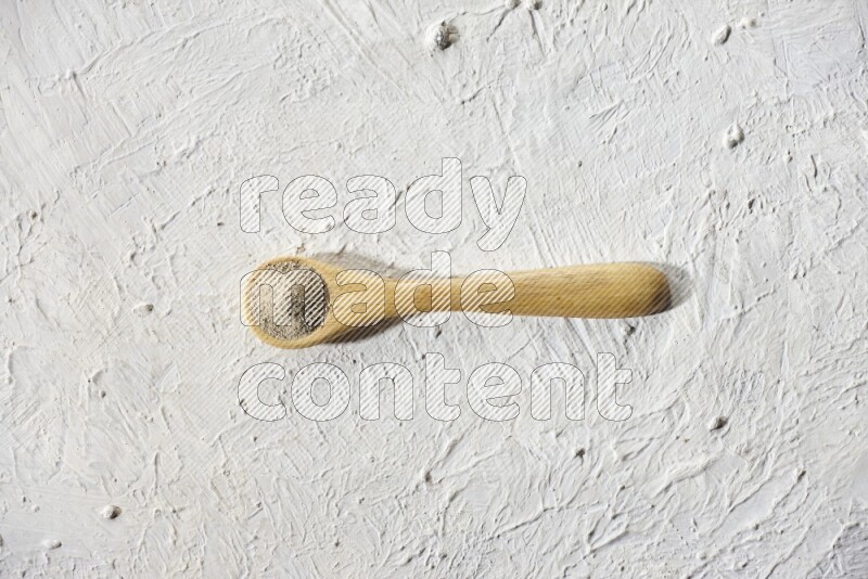 A wooden spoon full of white pepper powder on textured white flooring