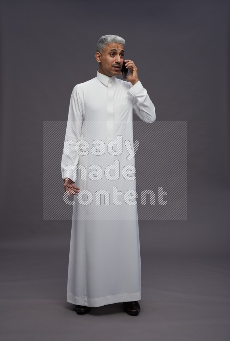 Saudi man wearing thob standing talking on phone on gray background