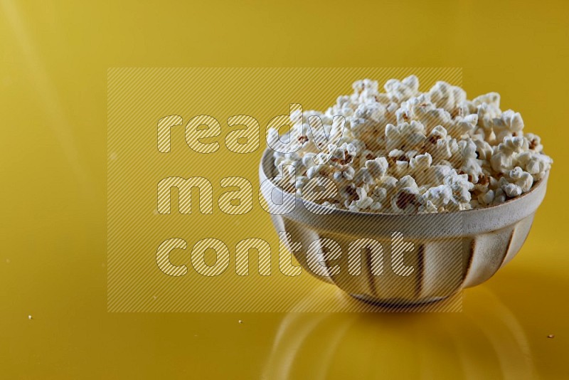 A white pottery bowl full of popcorn on a yellow background in different angles