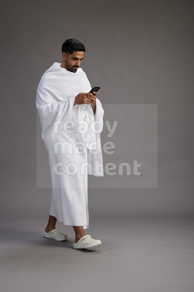 A man wearing Ehram Standing texting on phone on gray background
