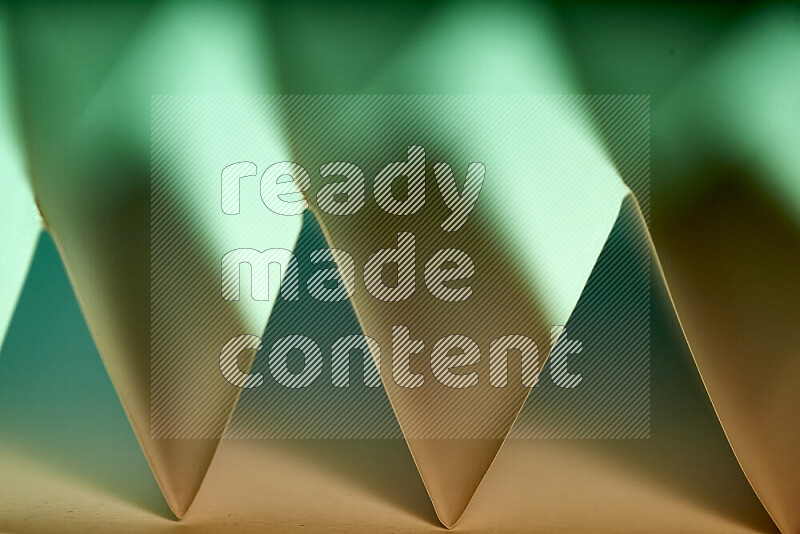 A close-up abstract image showing sharp geometric paper folds in green gradients and warm tones